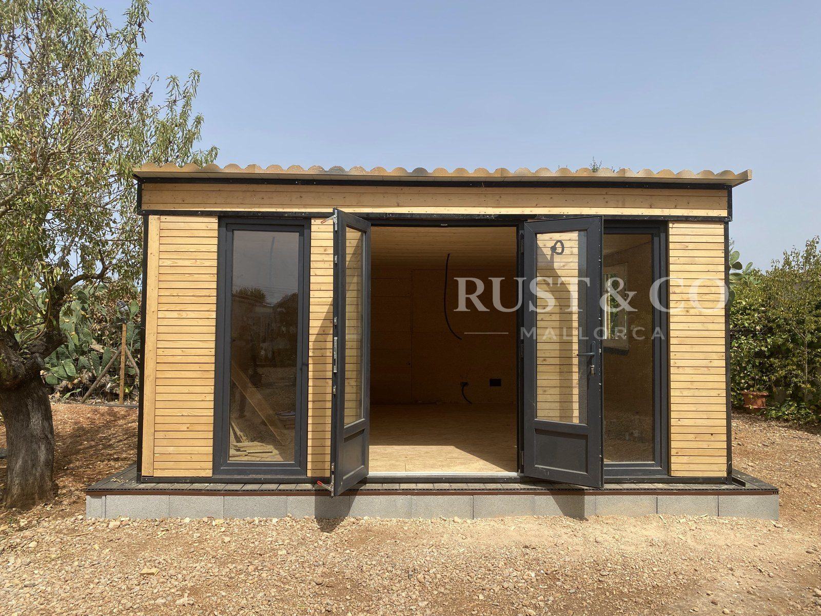 Casa de madera con grandes puertas acristaladas junto a un olivo en Mallorca
